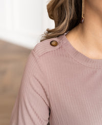 Woman in a bamboo T-shirt, dusty pink, with brown shoulder buttons.