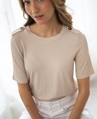 Woman wearing a light sand bamboo T-shirt, sitting and smiling softly in bright natural light.