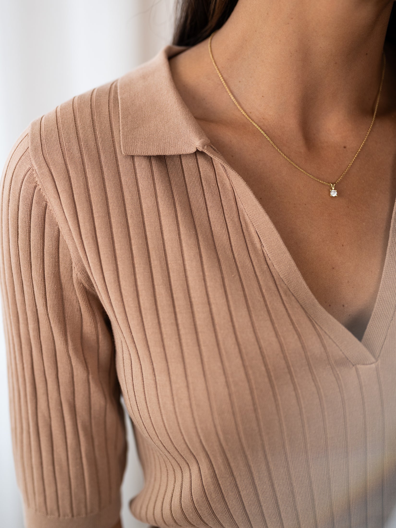 Woman wearing a sand-colored Tencel-silk polo shirt, shown from shoulders to chest.