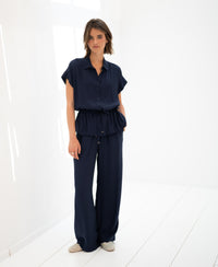 Dark blue LA LYNETTE trousers by OVERIG, shown from the front in a bright white minimalist room.