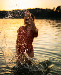 Terra-colored LA JODY blouse by OVERIG shown by the lake at sunset.