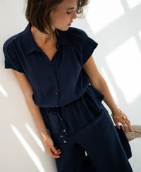 Woman wearing a dark blue LA JODY blouse stands by a sunlit white wall.