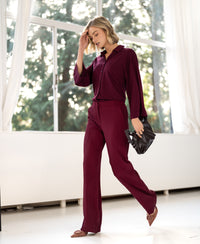 Woman in the flowy LA JOELLE trousers from PLEIN PUBLIQUE standing in sunlight near large windows.