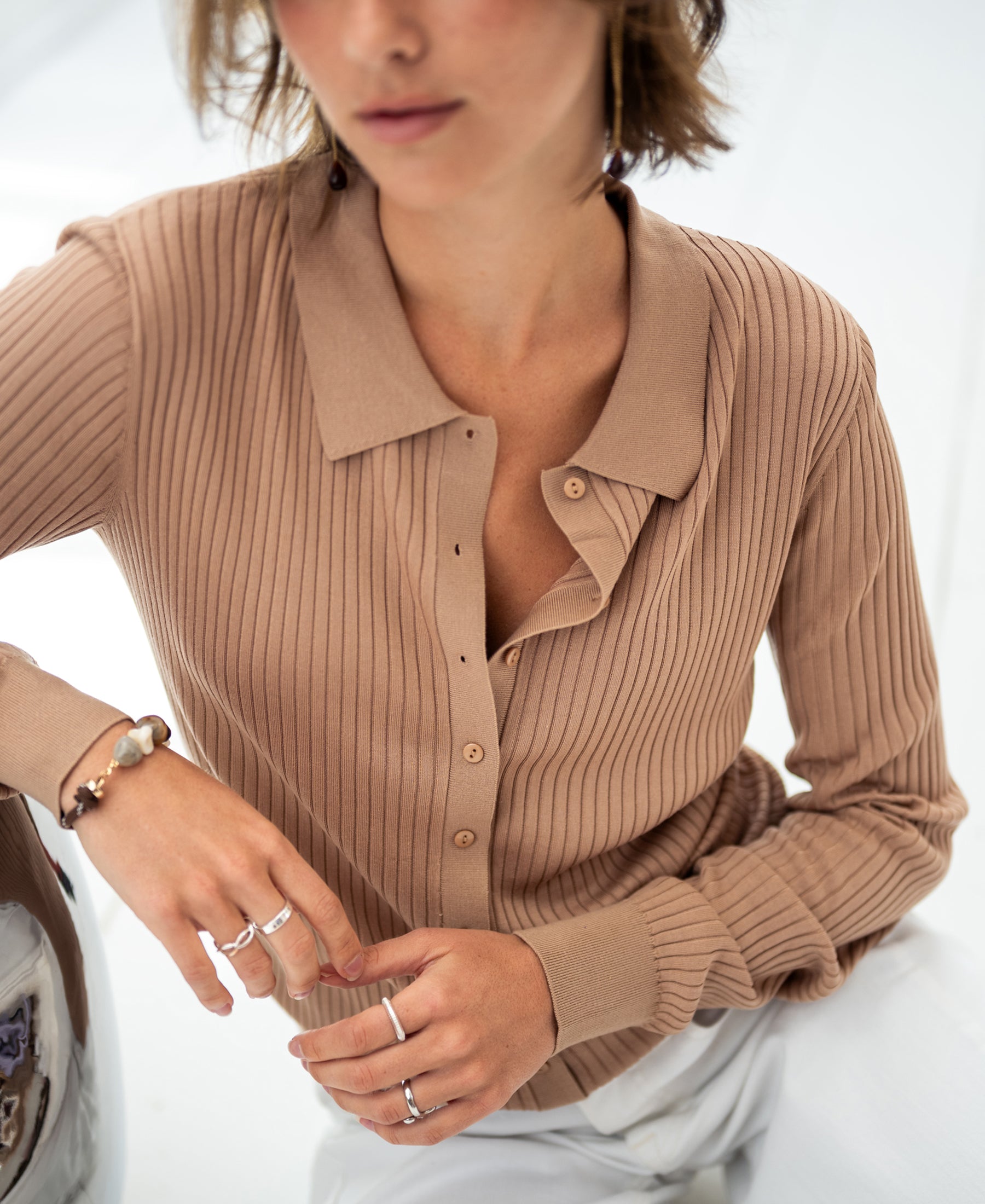 Woman wearing a sand-colored Tencel-silk ribbed cardigan, seated in a relaxed pose.