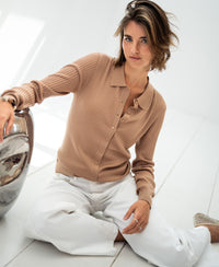 Woman wears a sand-colored Tencel-silk ribbed cardigan on a sunlit white floor.
