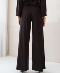 Back view of PLEIN PUBLIQUE LA JULIA Travel Pants in Pure Choco, worn by a person indoors.