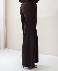 Pure chocolate brown travel pants in a minimal, light room.