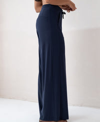 Navy blue LA JULIA travel pants by PLEIN PUBLIQUE, shown from the side against a light wall.