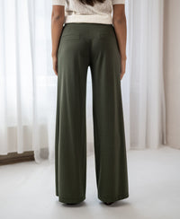 Back view of PLEIN PUBLIQUE dark olive travel pants LA JULIA, worn by a woman standing indoors.