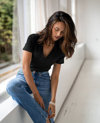 Woman wearing a black Lyocell T-shirt sits by a window, looking down.