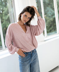 Woman wears the PLEIN PUBLIQUE wrap blouse LA LARA Dot in dusty pink and ivory, posing indoors.
