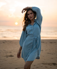 Tencel blouse dress in bleached color, shown on a sandy beach at sunset with the ocean in the background.