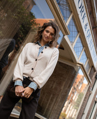 Woman wears a light sand-colored round-neck vest from PLEIN PUBLIQUE LA LEA collection outside a shop on a city street.