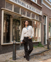 Woman wearing a light sand round-neck vest by PLEIN PUBLIQUE, shown walking past a Patchwork & Quilt Shop sign.
