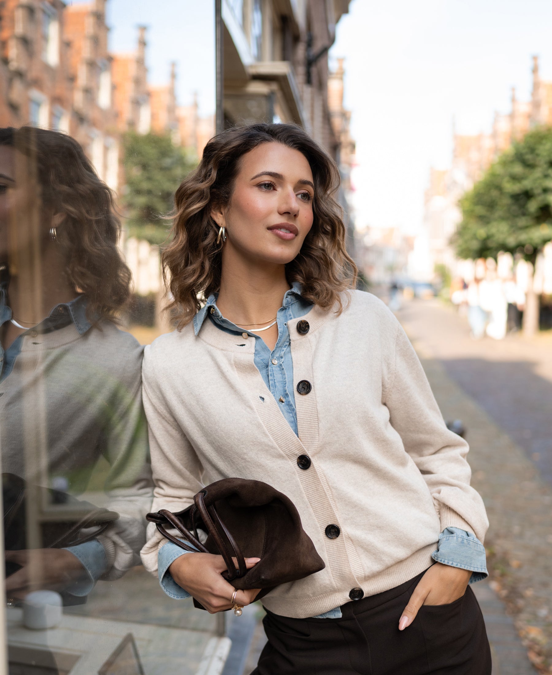 Woman wearing a PLEIN PUBLIQUE round neck vest in light sand stands by a window.