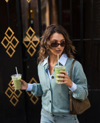 Woman wearing a light blue-green LA LEA vest from PLEIN PUBLIQUE, standing by a gate.