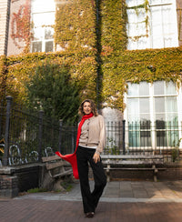 Coral-red merino wool wrap shawl shown outdoors near an ivy-covered building.