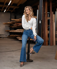 Woman wearing stonewash wide leg jeans, sitting on a workshop stool and smiling.