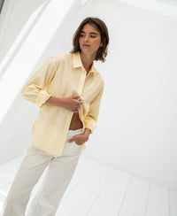 Soft yellow oversized easy-iron blouse in a bright, minimalist room.