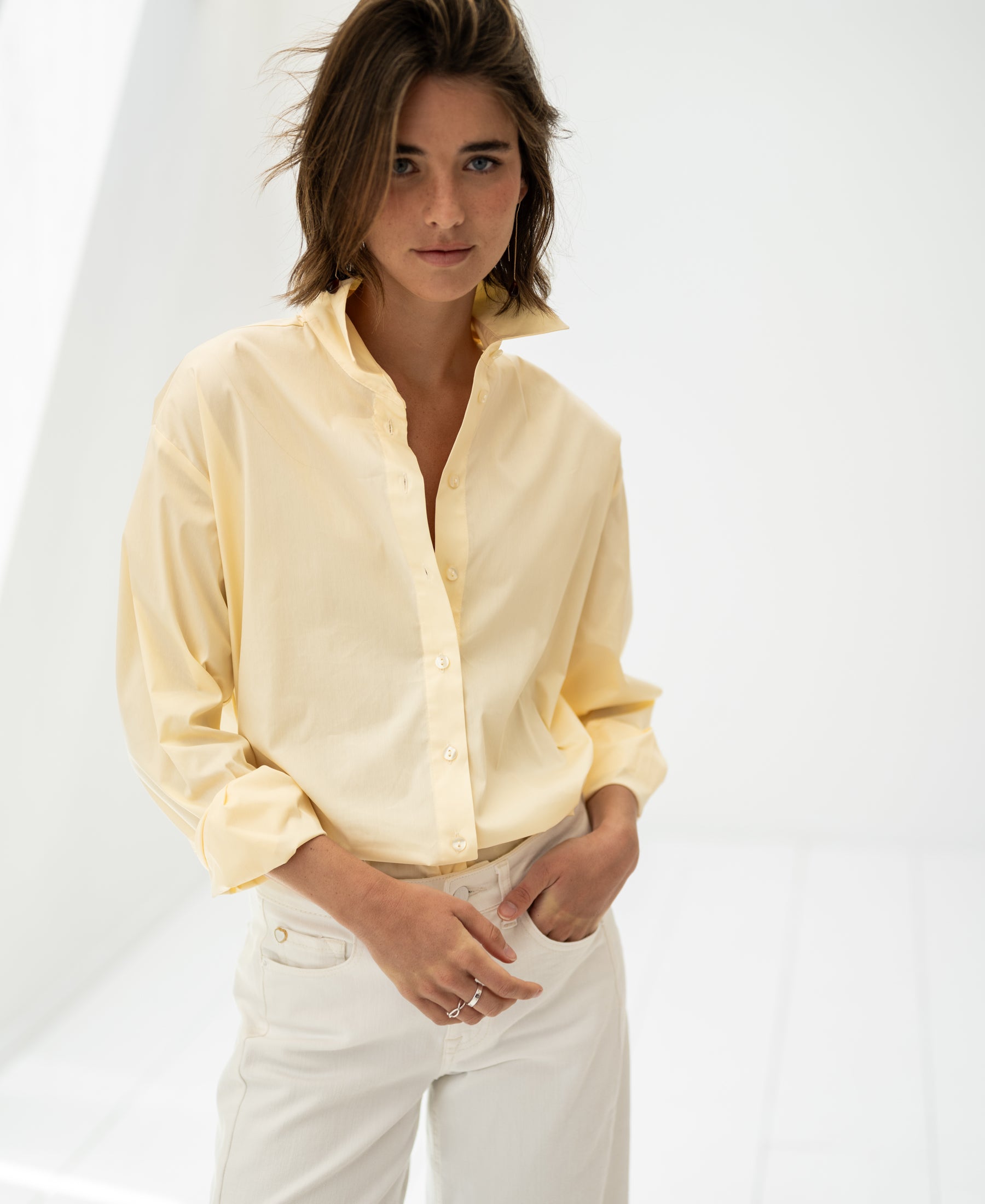 Woman wears PLEIN PUBLIQUEs oversized easy-iron blouse in soft yellow.