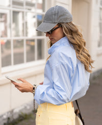 Woman wearing an oversized light blue blouse stands outside.