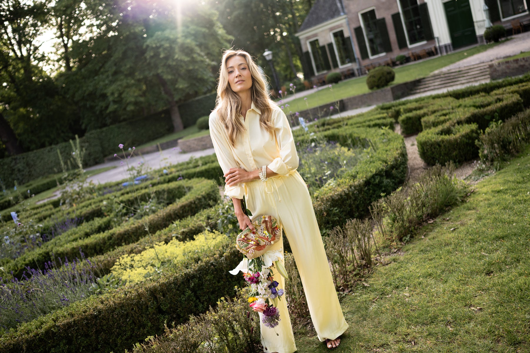 Yellow LA Lynette trousers by OVERIG, shown worn by a woman standing outdoors in sunlight.