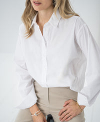 Woman wears an oversized easy-iron white blouse from PLEIN PUBLIQUE.