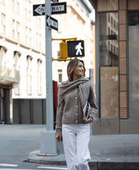Woman wearing a sand-colored mohair scarf crosses a city street, smiling.