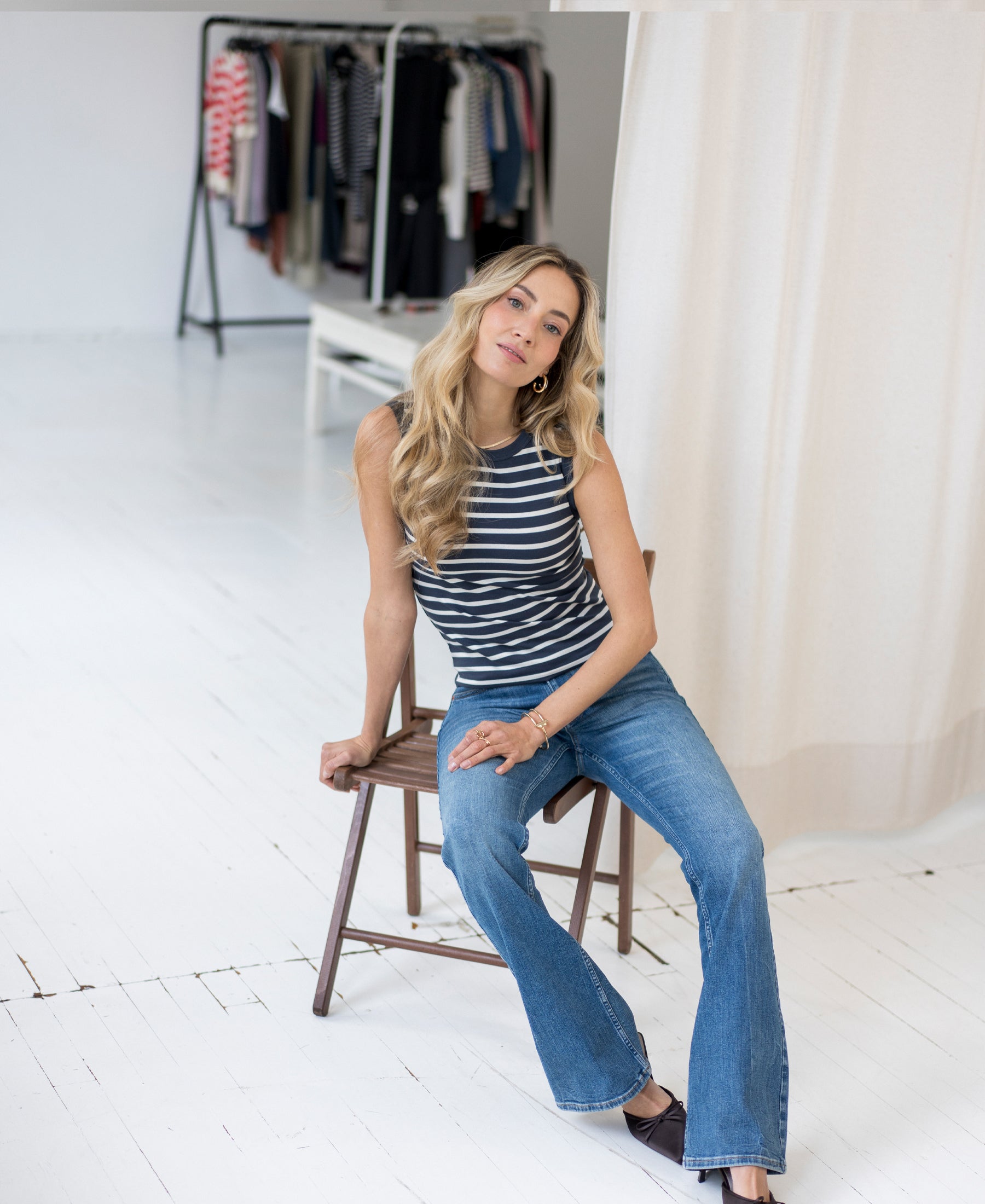 Woman wears blue flared jeans in a stonewash finish, seated in a bright room.