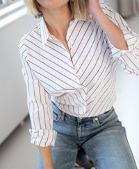 Woman wearing a PLEIN PUBLIQUE striped blouse LA LOIRE in ivory white and wine red, seated on a chair.