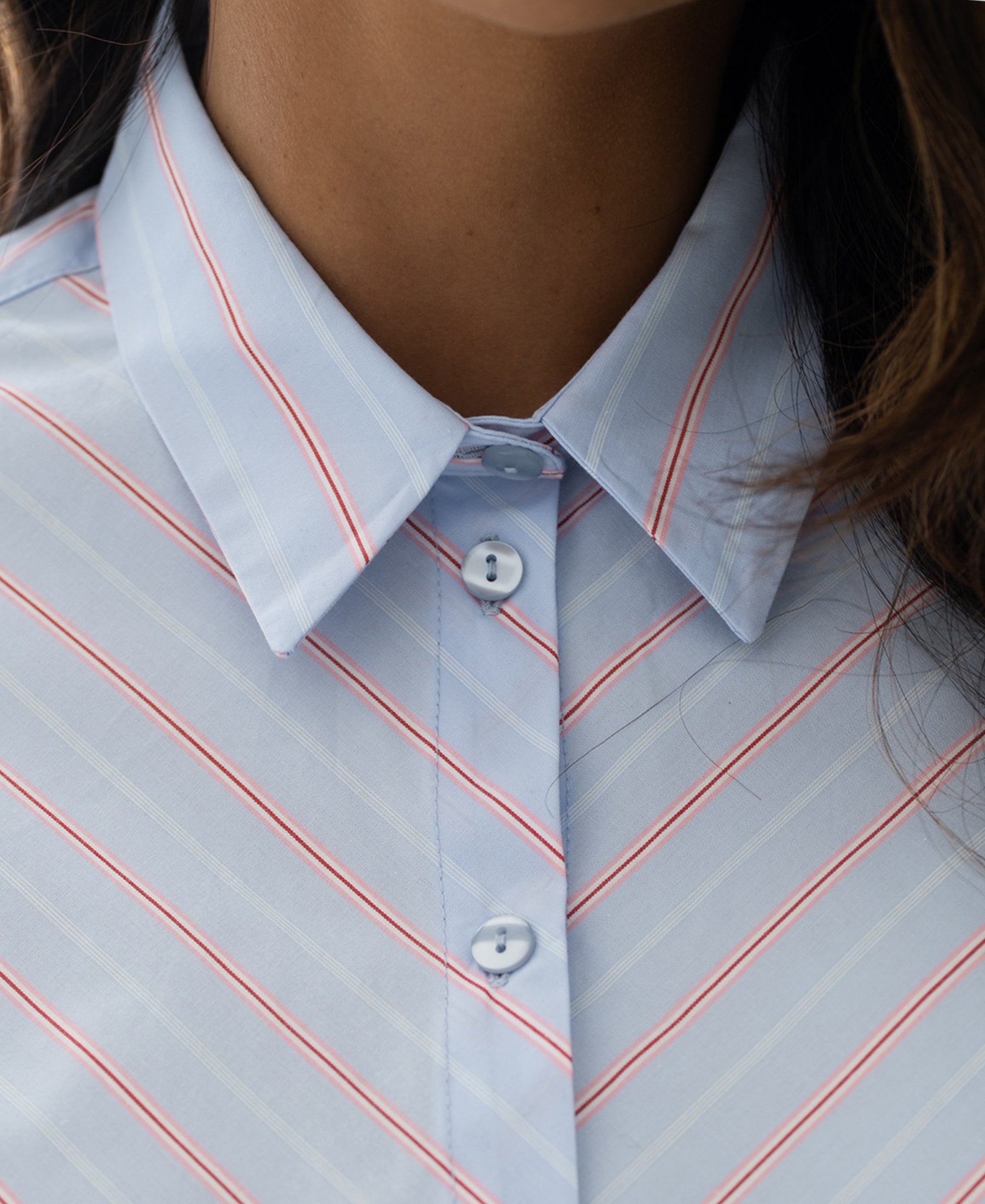 Close-up of the PLEIN PUBLIQUE striped blouse The Loire in light blue and coral, buttoned to the collar.