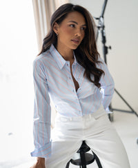 Woman wearing a light blue and coral striped blouse sits indoors.