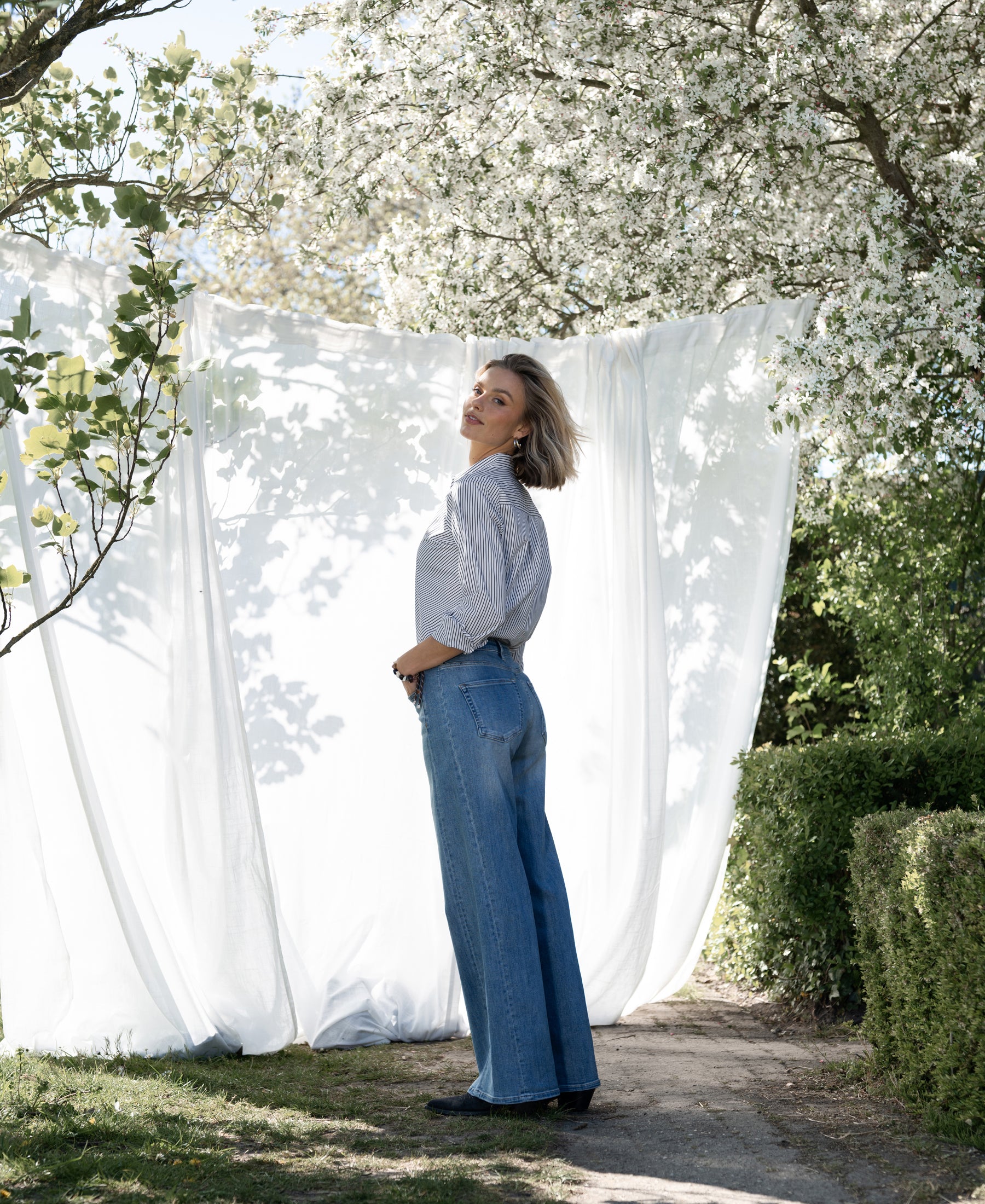 Striped Blouse LA LOIRE White-Black by PLEIN PUBLIQUE, shown surrounded by flowering trees.