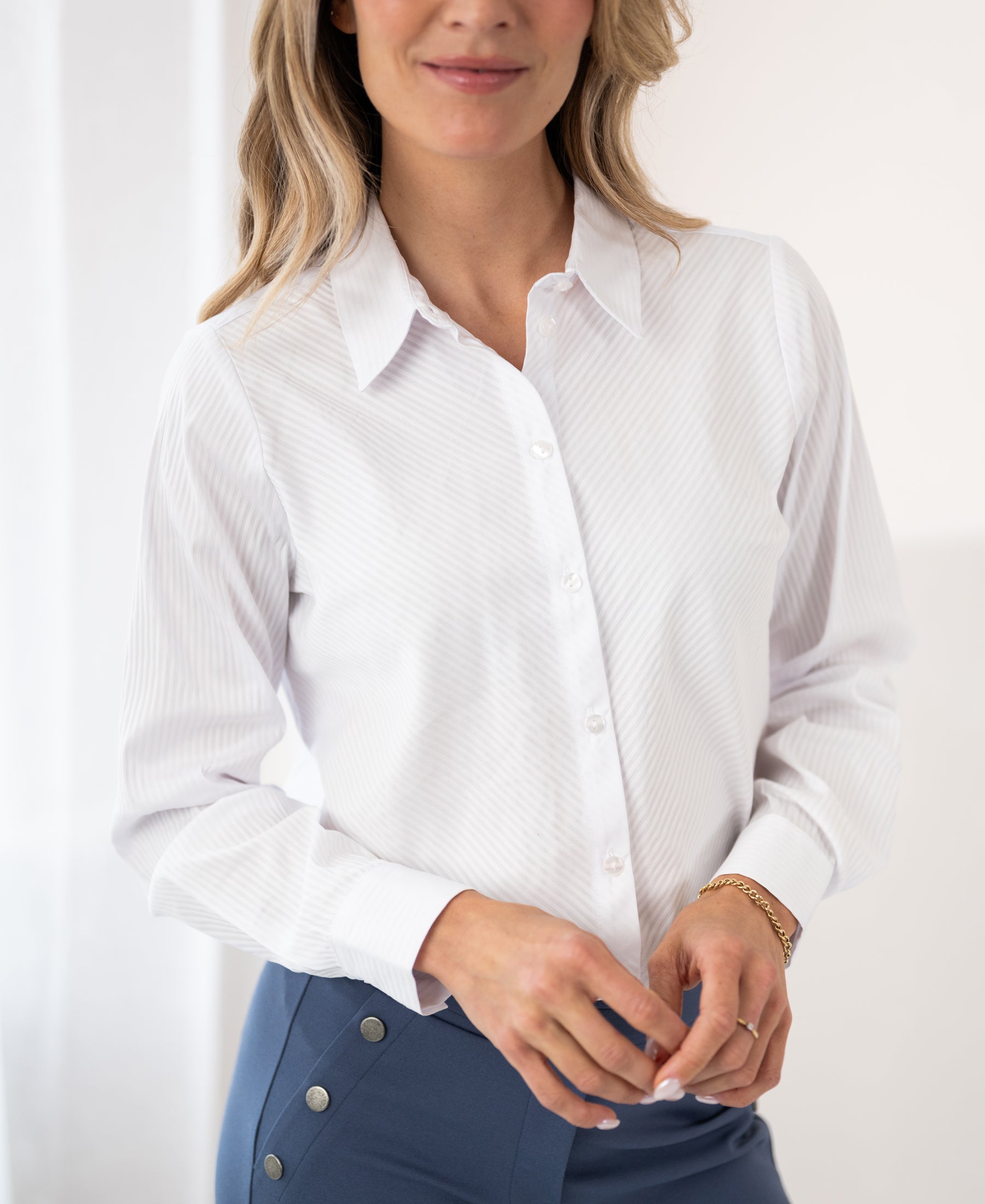 Woman wearing PLEIN PUBLIQUE LA LOIRE blouse in tone-on-tone white stripes, smiling and relaxed indoors.