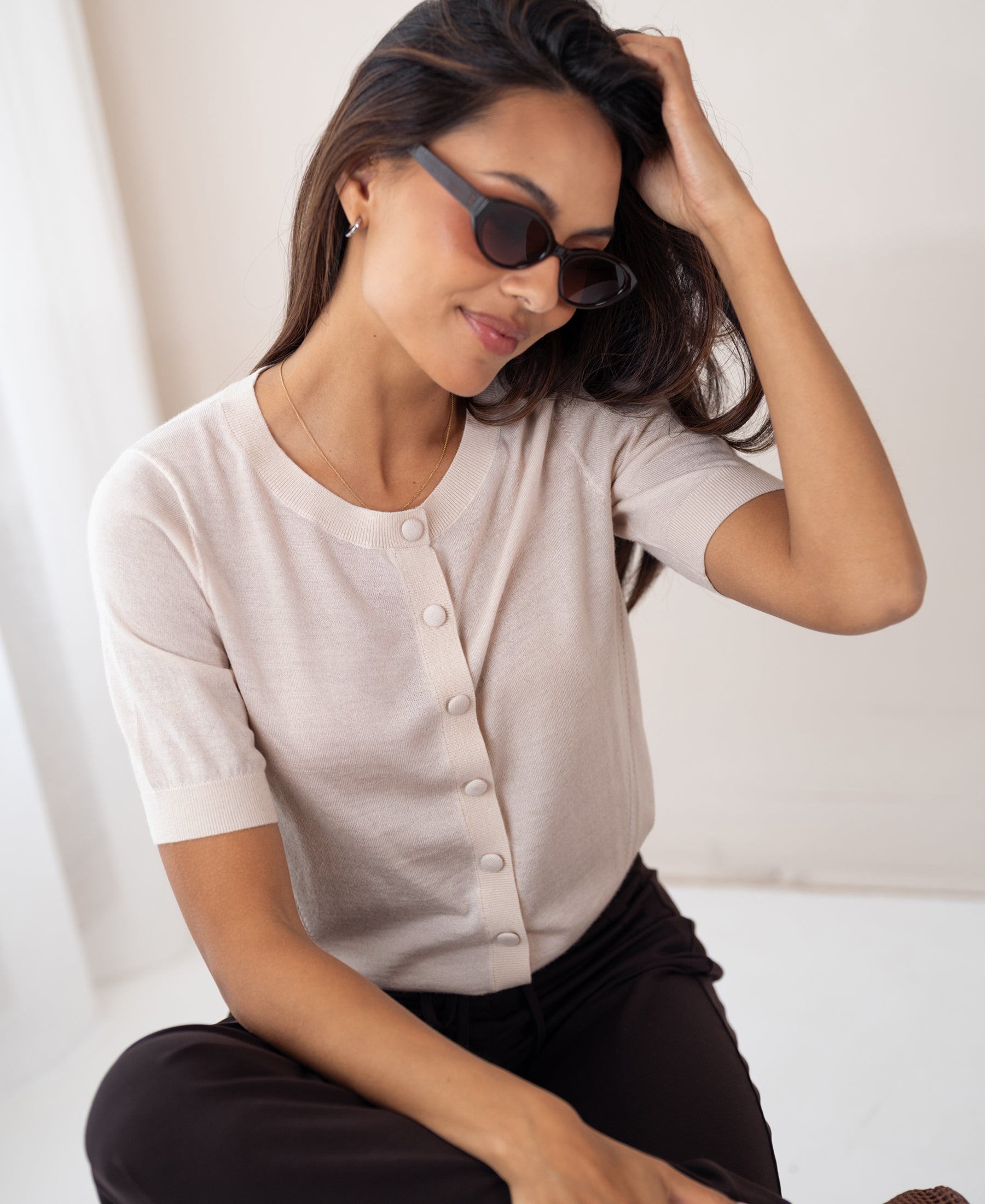 Woman wears a blush-colored merino wool and silk cardigan, smiling indoors.