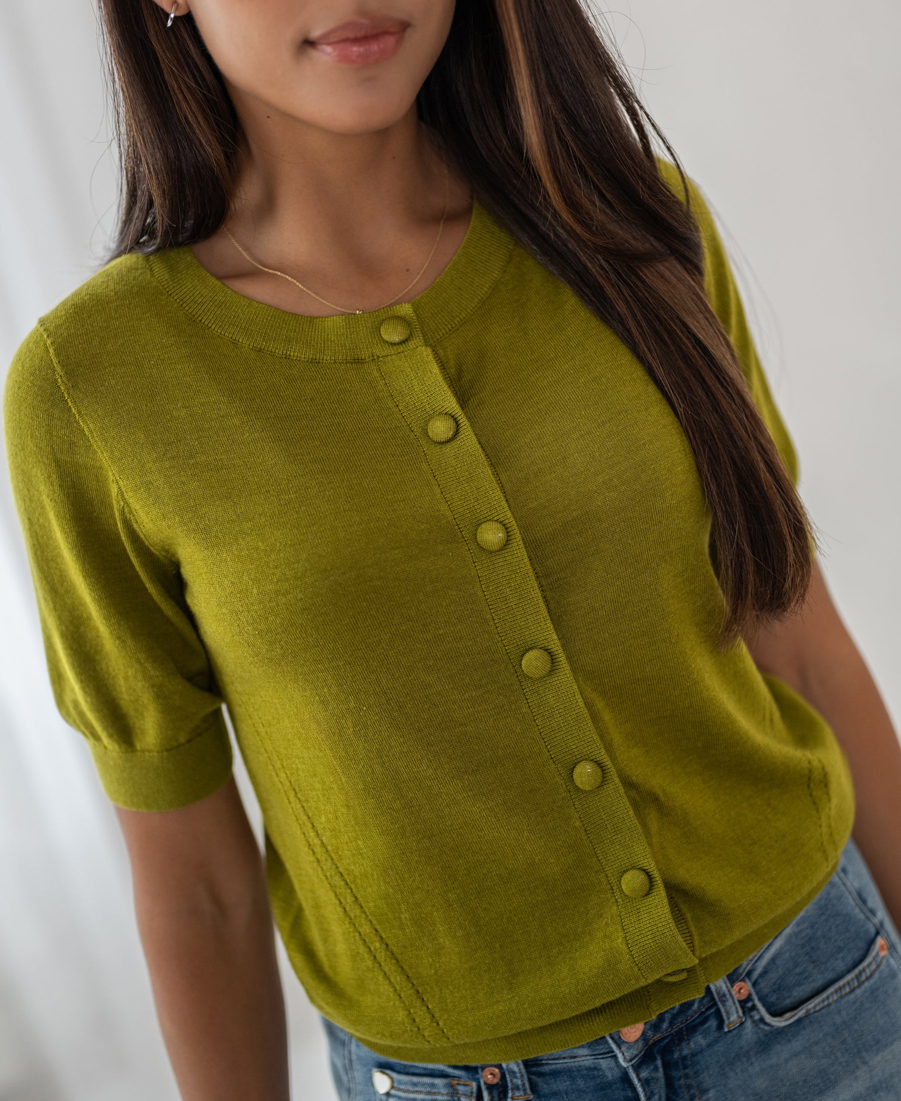 Woman wears an olive green merino wool and silk cardigan from PLEIN PUBLIQUE, style LA LORAINE, indoors.