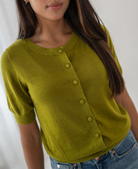 Woman wears an olive green merino wool and silk cardigan from PLEIN PUBLIQUE, style LA LORAINE, indoors.