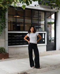 Woman wearing LE LOUIS silver-grey merino top standing outside in front of a modern building with large windows.