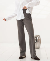 Person wearing knitted pants in dark sand color on a white floor.