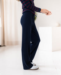 Person wearing dark blue PLEIN PUBLIQUE knitted trousers in a sunlit room.