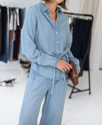 Woman wearing light blue Tencel denim blouse in a bright room.