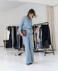 Front view of woman wearing a Tencel denim blouse by PLEIN PUBLIQUE in a bright room.
