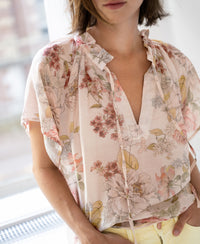 Blush floral print blouse with LA LUNETTE design shown indoors near a window.