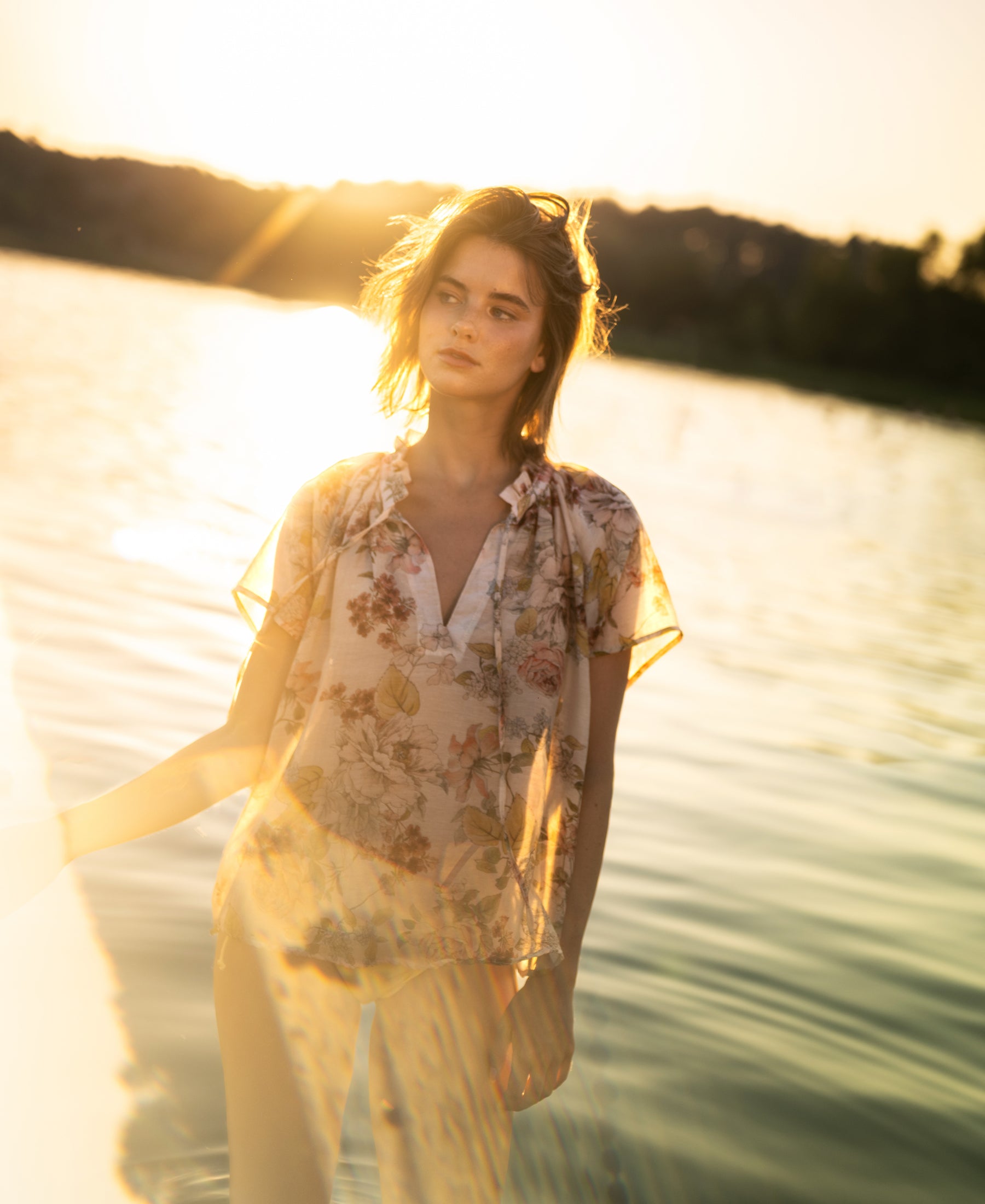 Blush floral print blouse top with butterfly sleeves shown at sunset in shallow water.