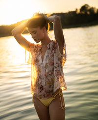 Blush floral-print blouse by PLEIN PUBLIQUE shown outdoors at sunset, front view.