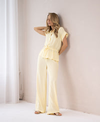 Light yellow LA LYNETTE pants shown on a woman standing against a white wall.