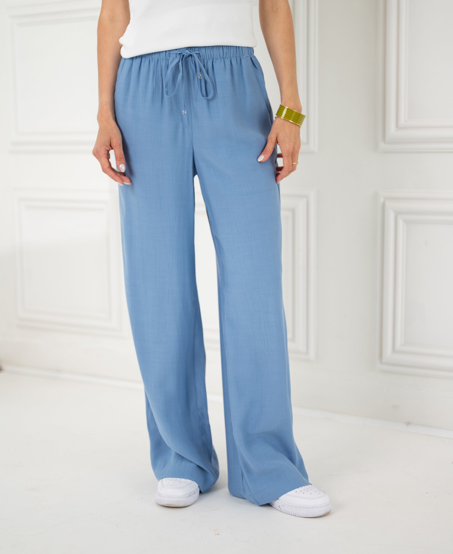 Person wearing LA LYNETTE Jeansblue pants stands indoors.