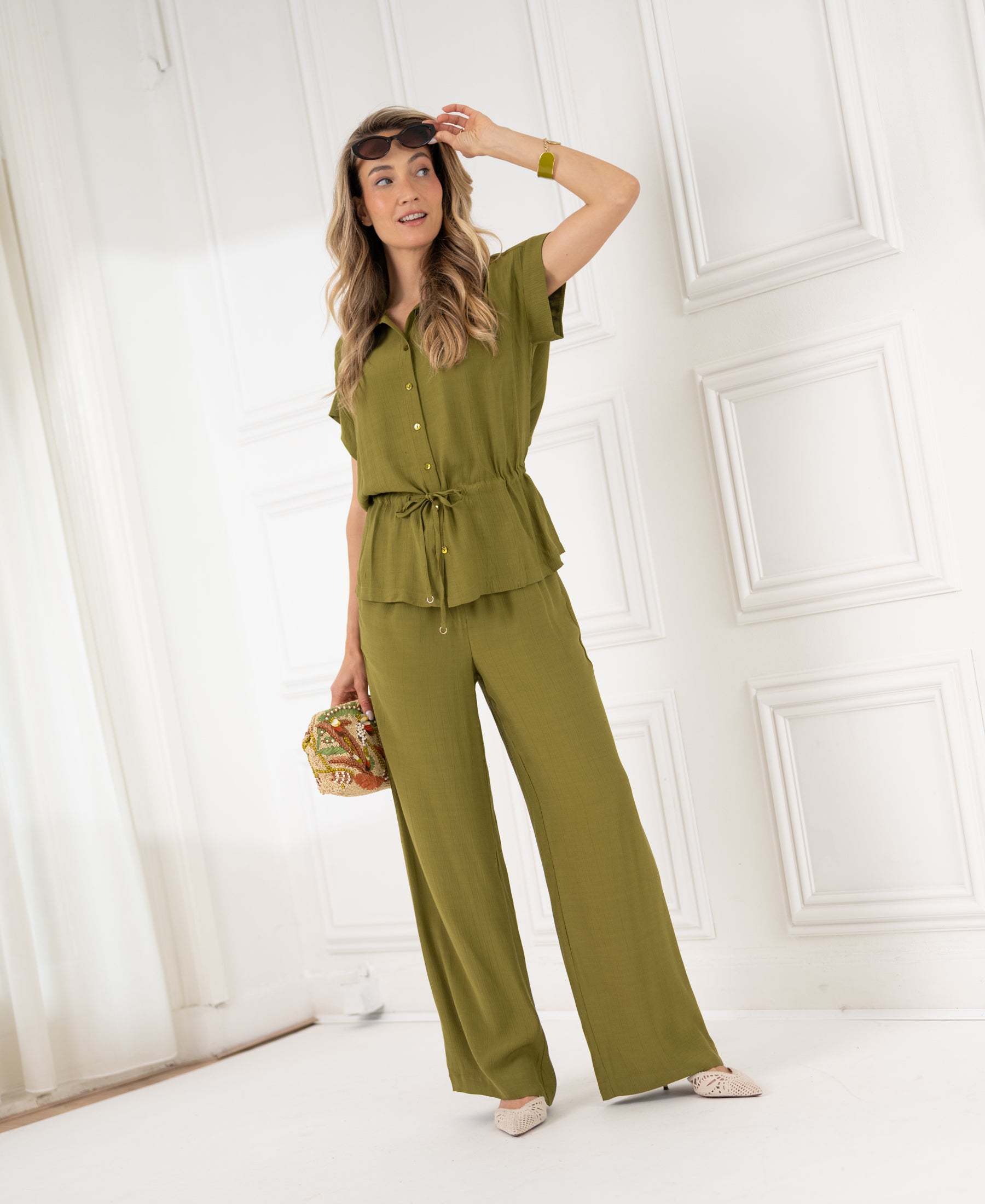 Woman wearing olive green LA LYNETTE pants stands indoors, looking to the side.