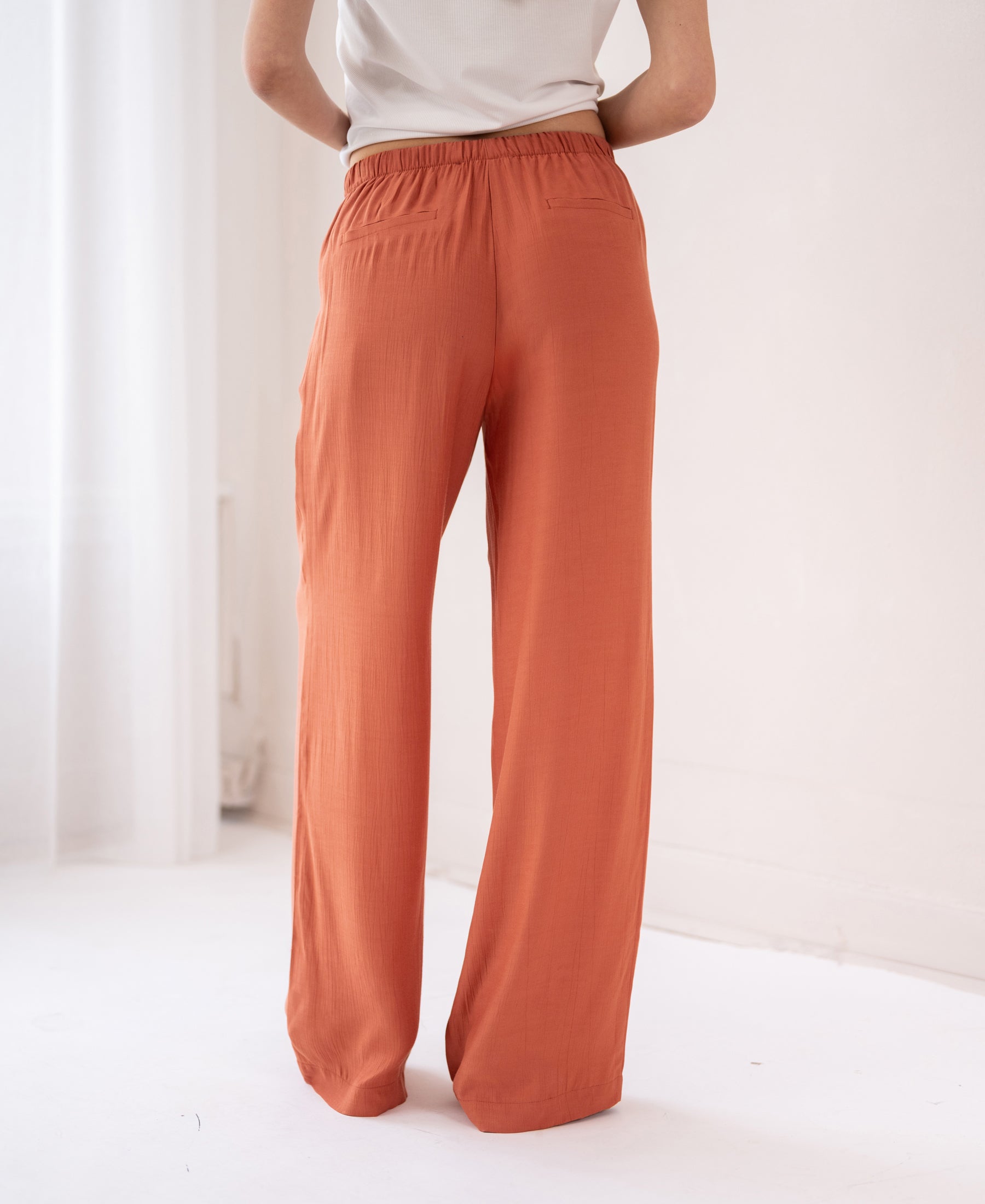 Wide leg orange viscose pants, waist down, shown indoors.