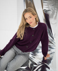 Merino wool vest in cassis color, shown worn by model sitting on reflective surface, facing the camera.